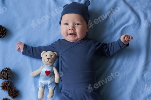 Preview: baby boy 3 months lies and smiles and holds a small toy bear in his hands.