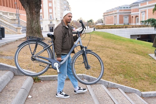 Preview: Stylish man carrying his bicycle up the stairs in the city