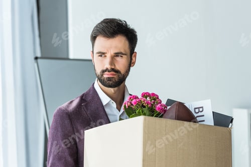 Preview: depressed young businessman carrying box of personal stuff after he gets fired