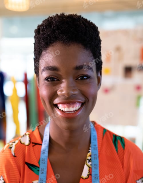 Preview: Smiling fashion designer wearing vibrant dress with measuring tape in studio