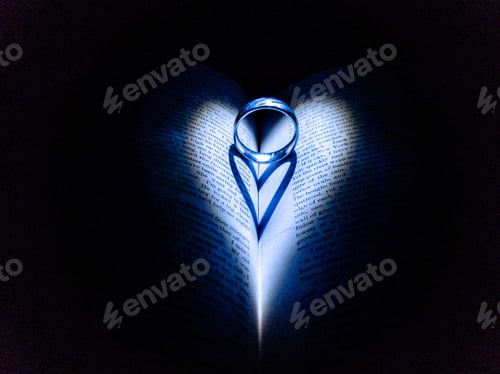 Preview: Closeup shot of a ring on a book with a heart-shaped shadow on a black background
