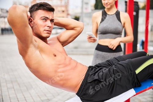 Preview: Muscular handsome guy doing abs crunches outdoors