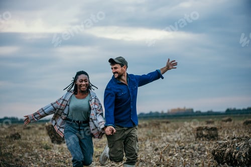 Preview: Happy farmers running through harvested field holding hands
