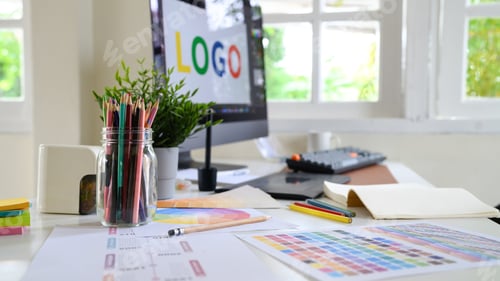 Preview: Creative woman designing logo sketches on notebook with color samples and tools