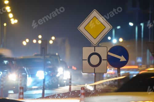 Preview: Roundabout road signs with blurred cars on city street traffic at night.