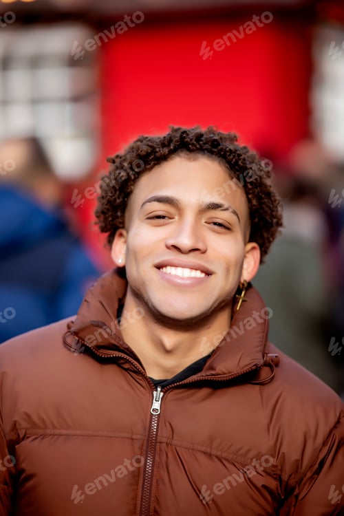 Preview: Young man smiling confidently with natural curly hair at a festive red market background.