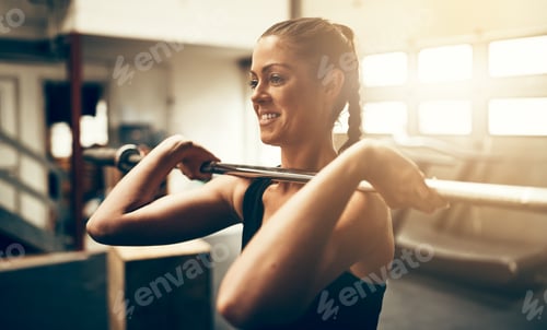 Preview: Fit young woman smiling and lifting weights in a gym