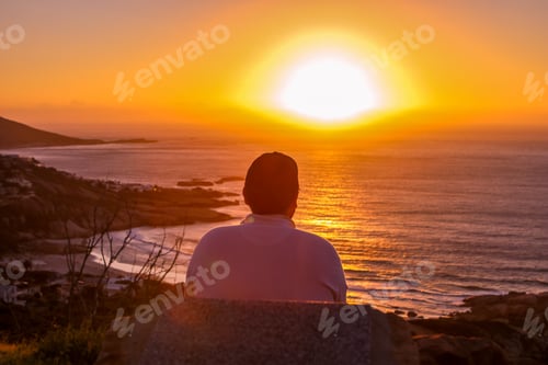 Preview: Man sitting at the cliff of Atlantic Ocean shore looking at beautiful sunset enjoying beauty and