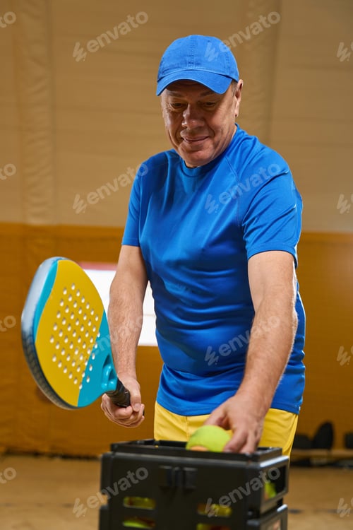 Preview: Man stands on a sandy field with a racket in his hands and takes a tennis ball