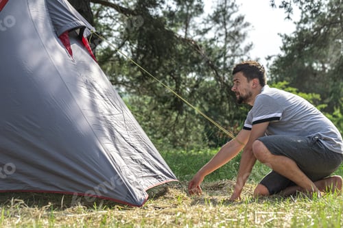Preview: Man putting up a tent in the forest.
