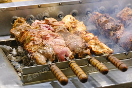 Preview: Succulent meat skewers grilling over hot charcoal with rising smoke on a metal barbecue grill.