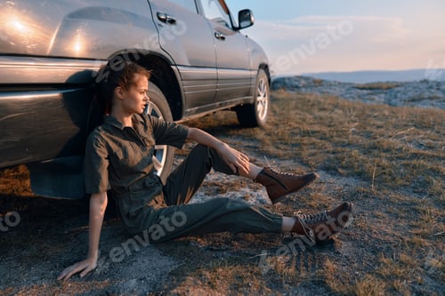 Preview: Traveler resting on the ground next to car during a road trip vacation in nature