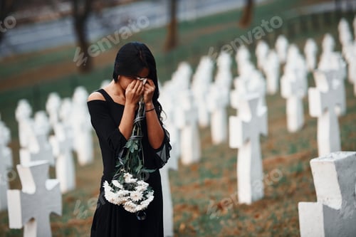Preview: Young woman in black clothes visiting cemetery with many white crosses