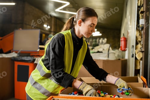 Preview: Young female worker of garbage sorting center wearing protective clothing and gloves while working