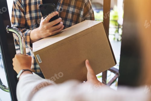 Preview: Closeup image of a woman receiving parcel box from delivery man at the house's door