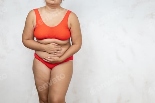 Preview: Naked overweight woman bending over touch stomach, white background. Woman in red underwear with