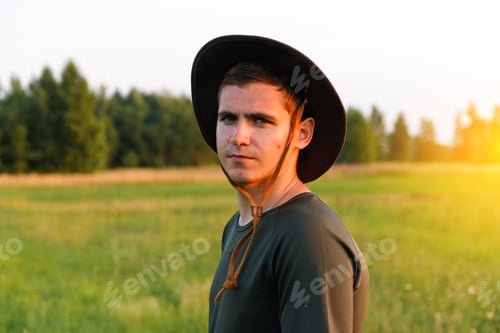 Preview: Young man farmer in cowboy hat at agricultural field on sunset with sun flare. Portrait of millennia