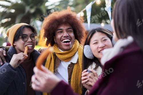 Preview: Laughing young people eating chocolate with churros together on street outdoors. Multiracial group.