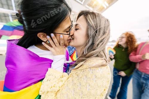 Preview: Young female couple in love kissing during gay pride parade festival day