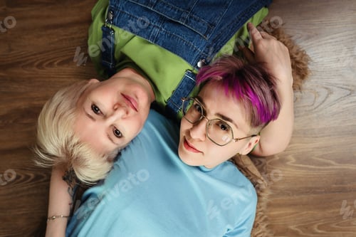 Preview: Smiling adult mother and daughter lie on floor next to each other at home