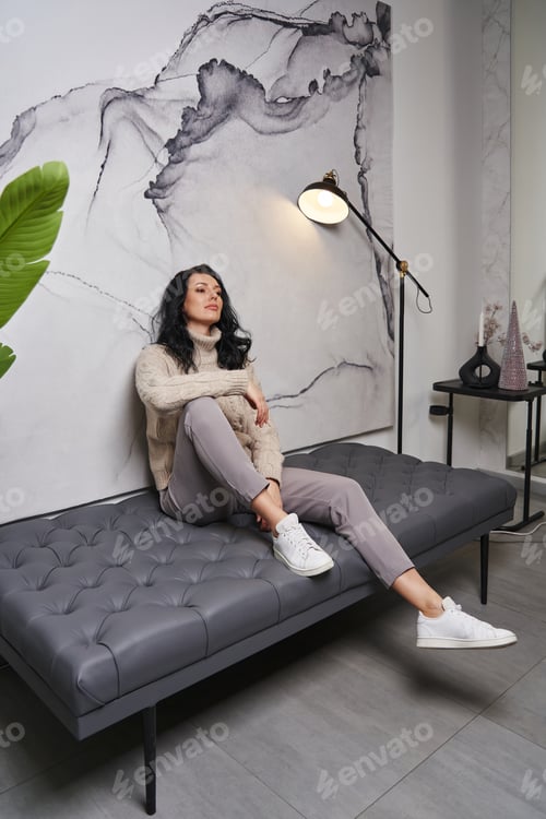 Preview: A young beauty dressed in a beige sweater and trousers decorates a chic interior while sitting on a