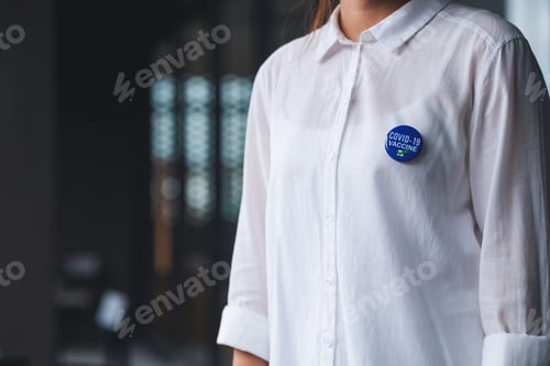 Preview: Closeup image of a woman with Covid-19 vaccinated sign brooch on shirt