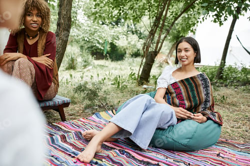 Preview: positive interracial girlfriend in boho styled outfits talking outdoors in retreat center