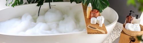 Preview: Modern bathroom interior with white bubble filled bathtub and monstera tropical plant. Eco body care