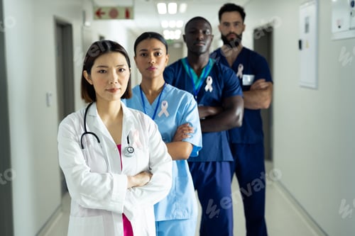 Preview: Portrait of diverse group of healthcare workers wearing cancer ribbons standing in hospital corridor