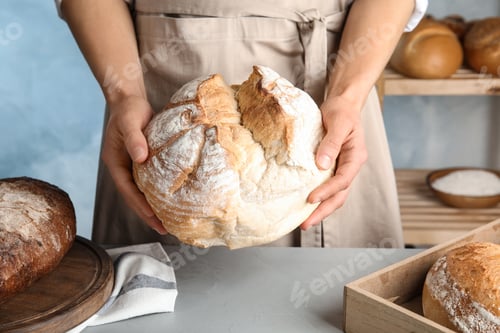 Preview: Baker holding loaf of bread over table indoors, closeup
