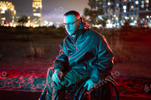 Preview: Pensive disabled young man taking walk outside in wheelchair, sits in red blue color rgb neon light.
