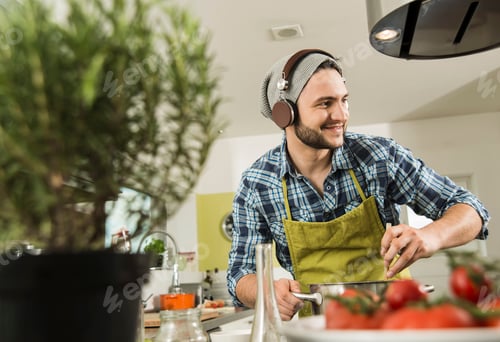 Preview: Young man with headphones cooking in kitchen at home