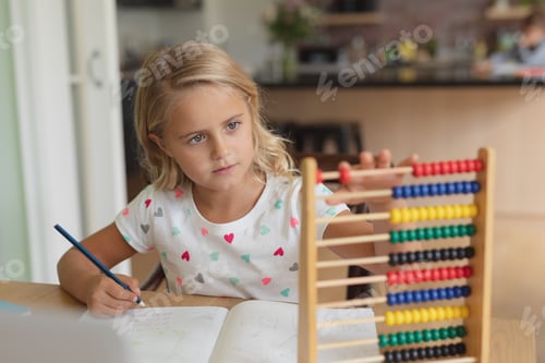 Preview: Front view of Caucasian girl doing homework at table in a comfortable home