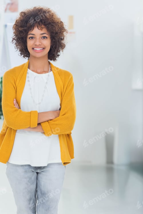 Preview: African American woman standing arms crossed in office wearing cardigan and necklace, copy space