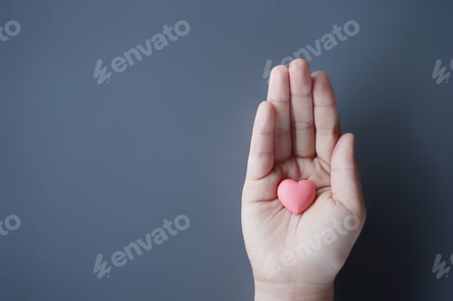 Preview: Small kid's hand holding pink heart with copy space.
