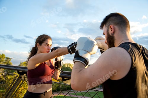 Preview: woman punching caucasian man with boxing gloves at sunset