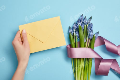 Preview: partial view of female hand with yellow envelope, and blue hyacinths with violet satin ribbon on