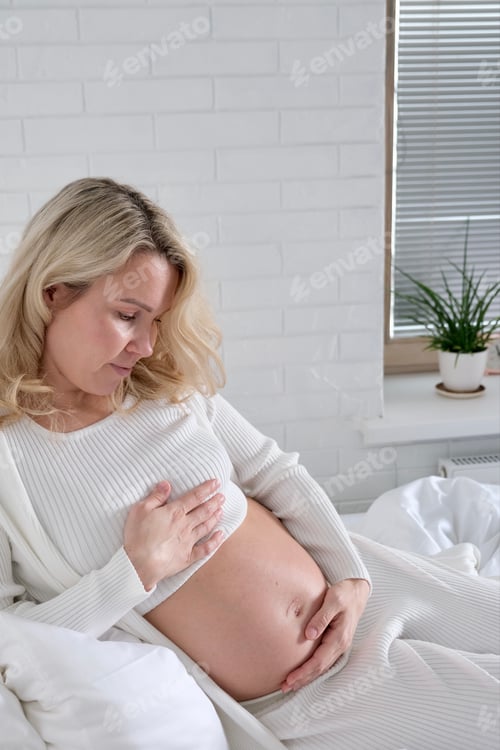 Preview: Pregnant Woman Holding Her Belly Relaxing Indoors