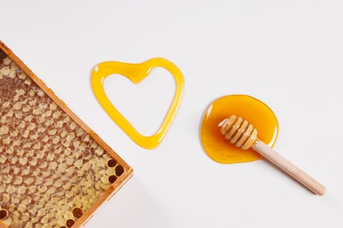 spoon with spilled honey and honeycomb on white background, top view