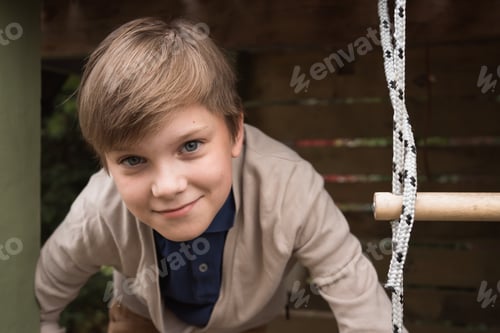 Preview: happy young boy climbing up a rope ladder playing in yard