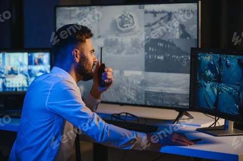 Preview: Back view of man watching surveillance footage and map on computers