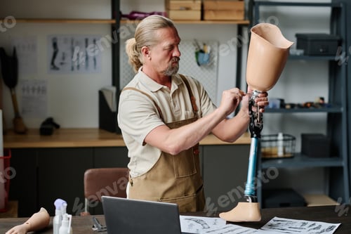 Preview: Senior craftsman building handmade leg prosthetics and screwing knee joint
