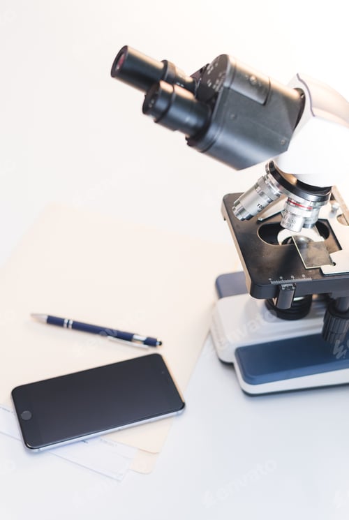 Preview: Close up of compound microscope on white lab desk with smartphone and pen on table