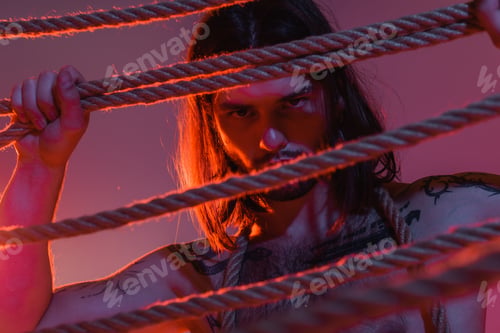 Preview: Shirtless tattooed model holding ropes on purple background with lighting