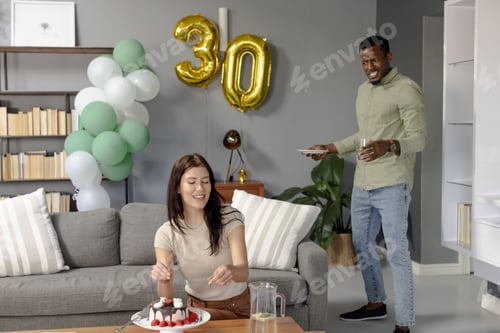 Preview: Celebrating 30th birthday, woman cutting cake while man bringing plates at home