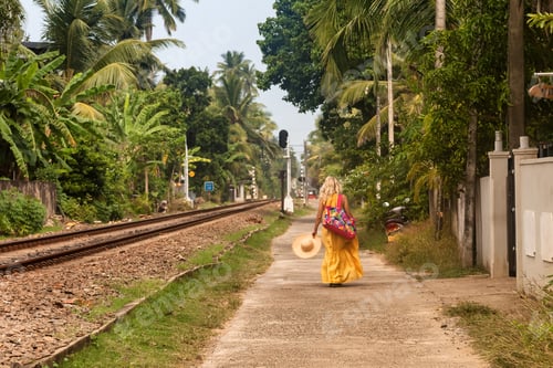 Preview: Rear view young woman wearing yellow dress walking on road at rural scene, from behind