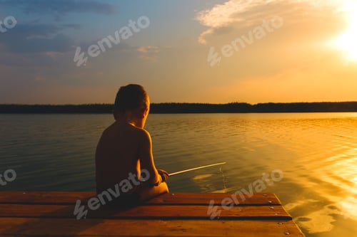 Preview: Little boy siting on wooden dock and fishing at sunset.