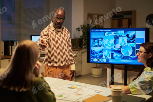 Preview: Senior Black Man Explaining Presentation to Young Women in Office