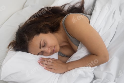 Preview: Tired woman sleeps on pillow under light blanket on bed in illuminated bedroom of modern apartment