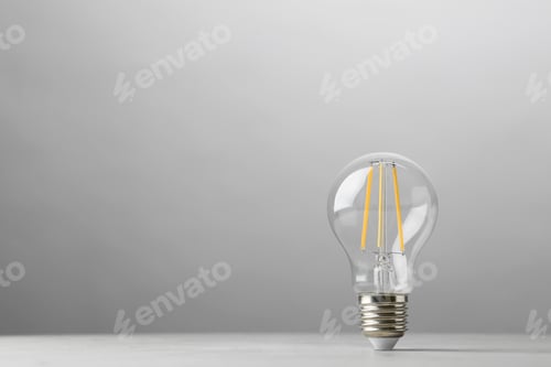 Preview: Vintage lamp bulb on light table against grey background. Space for text